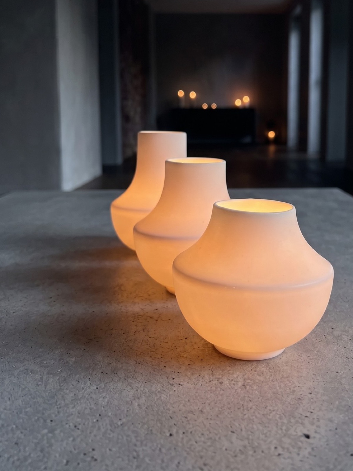 casting: drei leuchtende Windlichter in einer Reihe auf einem Betontisch