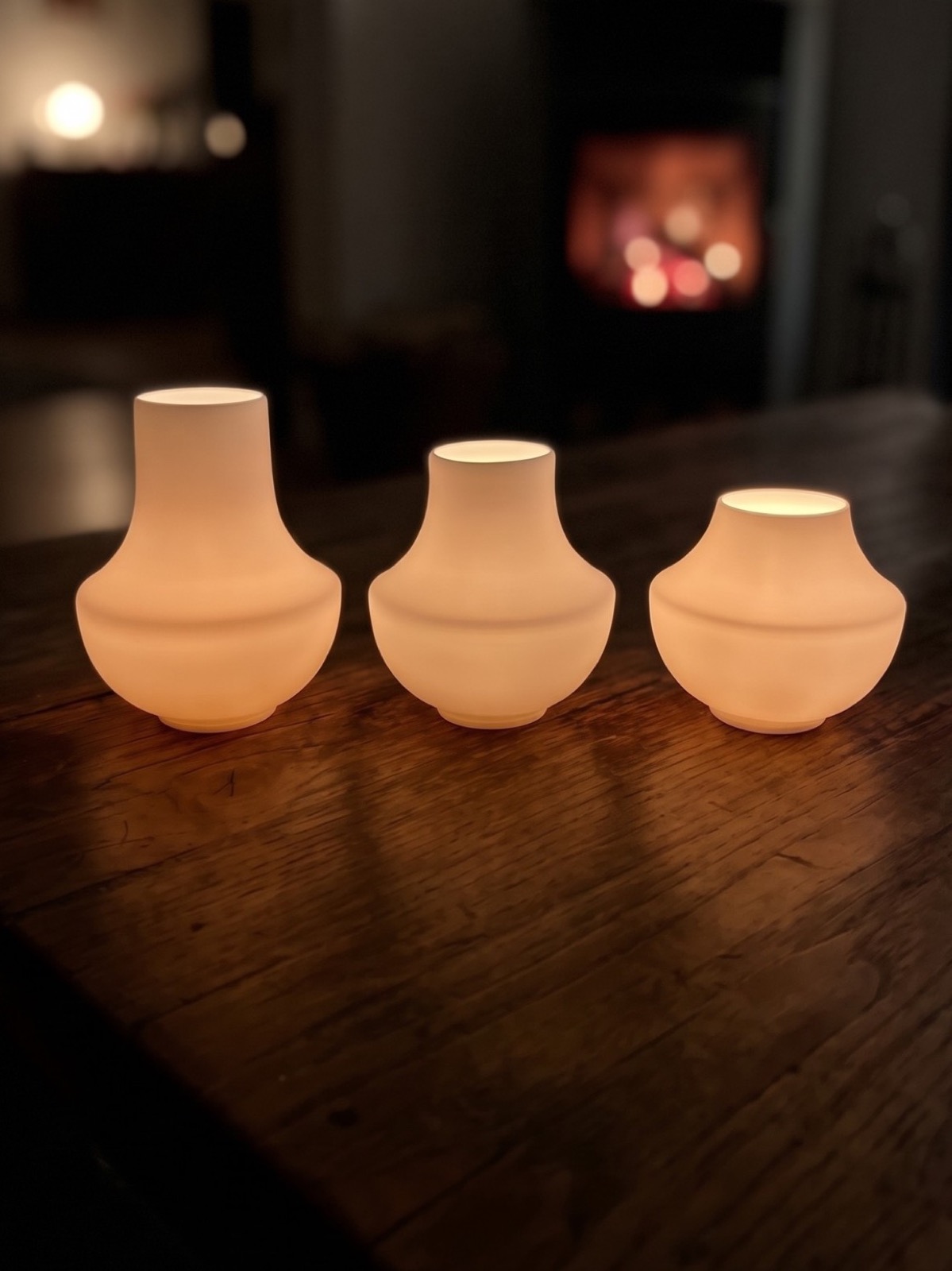 casting: drei Windlichter in drei Größen auf einem Holztisch vor einem Kaminfeuer