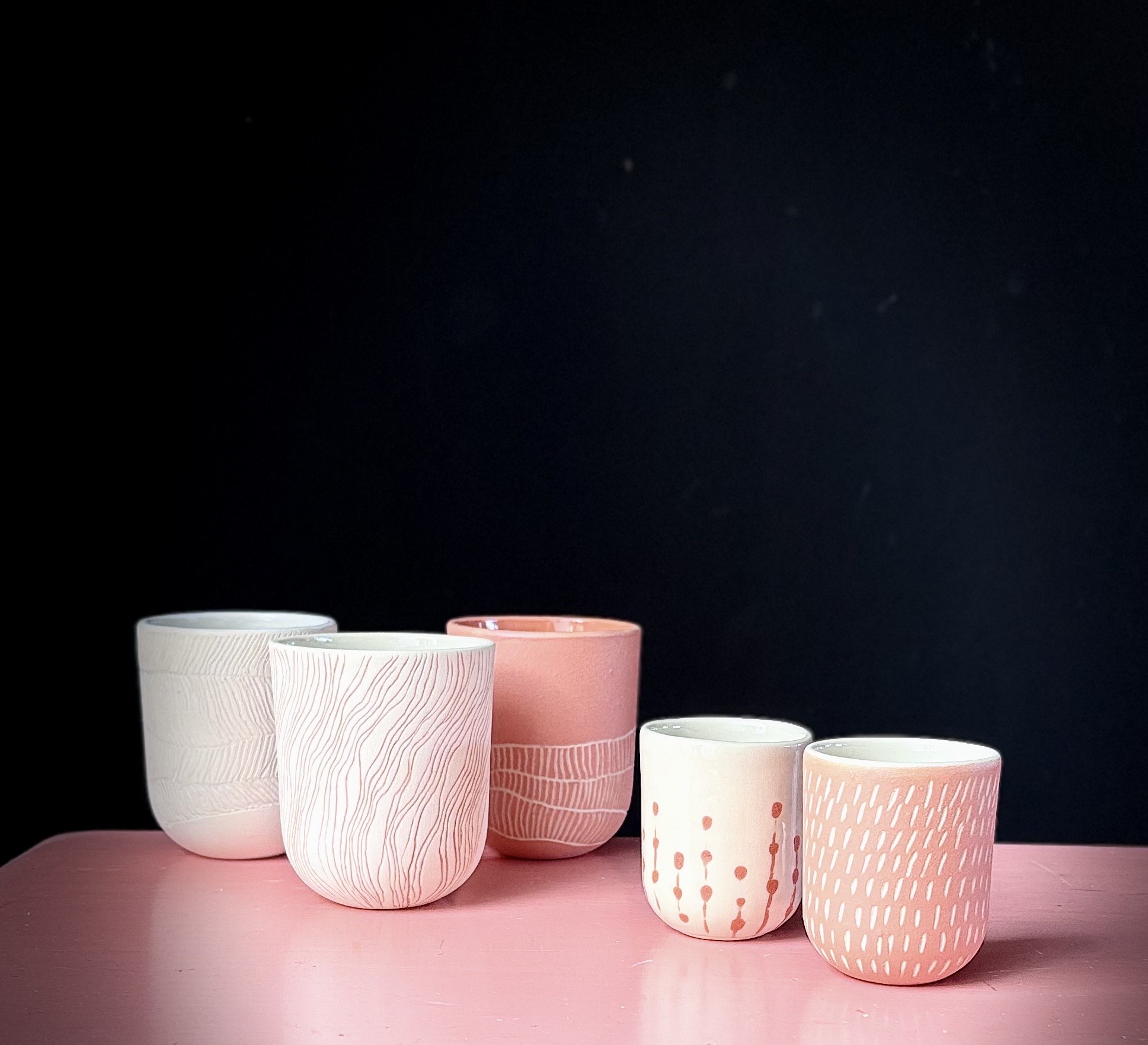 Handgestaltete Becher mit Sgraffito- und Engobe-Dekor auf einem rosa Tisch